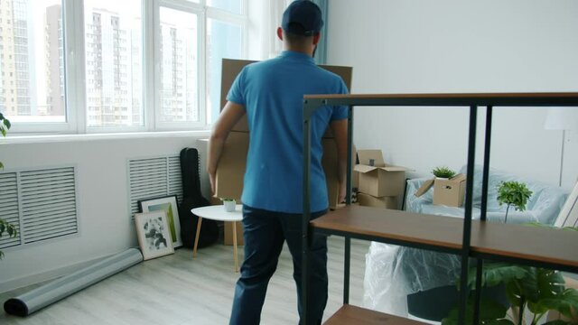 Portrait of young man mover delivering cardboard boxes to young woman's apartment helping with relocation. People and occupation concept.