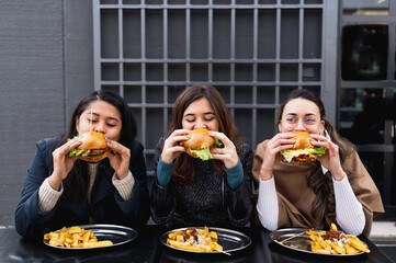 Females sitting at table restaurant biting burgers. Fast food unhealthy eating.