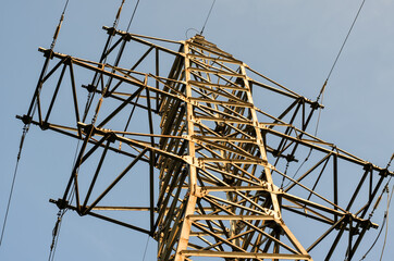 Part of  transmission tower (power tower) with powerful steel frame and high-voltage wires, angled view, sunny day, blue sky background