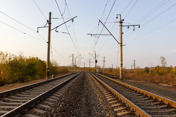 In the center there are parallel railway tracks and poles of electric wires extending into the distance at sunset