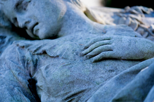 Fragment of an ancient statue of end of human life. Beautiful dead woman light on the bed. Selective focus on hand.