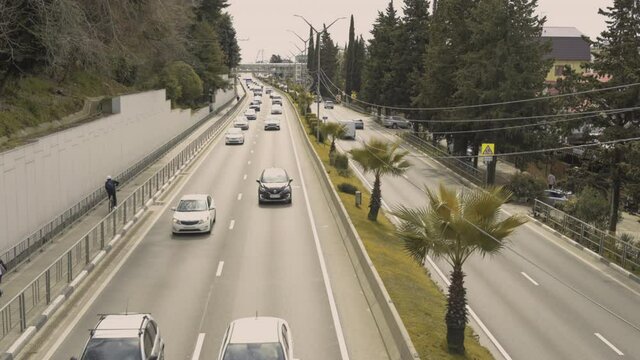 Timelapse of many cars passing by on the highway of a seaside city along a sidewalk with palm trees and landing plane. View from the bridge, top view