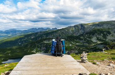 Fototapeta na wymiar A man with a full backpack and bedding on his sides stands on top of a mountain enjoying the breathtaking stunning scenery. Mountain lake view