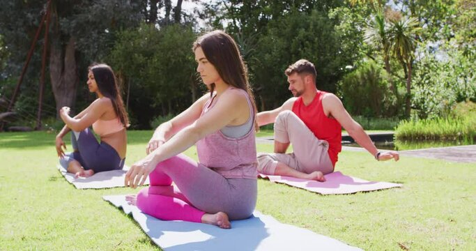 Diverse group of men and women practicing yoga sitting on mats in sunny park