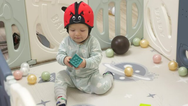 Cute toddler playing with soft montessori building blocks in baby playpen with play mat for babies and toddlers, 8 month old baby boy wearing safety helmet enjoy playing time in kids activity centre.