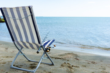summer chaise longue chair with a fishing rod for fishing on a sandy beach by the sea