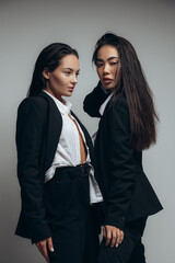 Two young women pose in studio standing in black suits.
