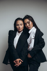 Two young women pose in studio standing in black suits.