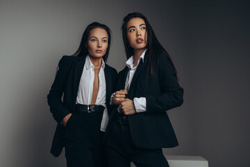 Two young women pose in studio in black suits.