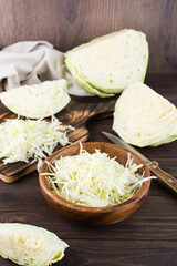 Fresh raw cabbage cut into strips in a bowl and pieces of cabbage on a wooden table. Vegetarian diet. Vertical view