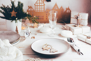 Organization of a festive Christmas table. Plate, cutlery, champagne glass and Christmas decorations. Tablescapes  on white wooden table