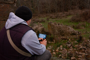A man sits with a phone and takes pictures of natural stones in the park