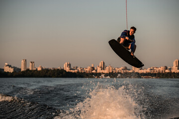 athletic man making trick in jump with wakeboard over splashing river. Summertime watersports...