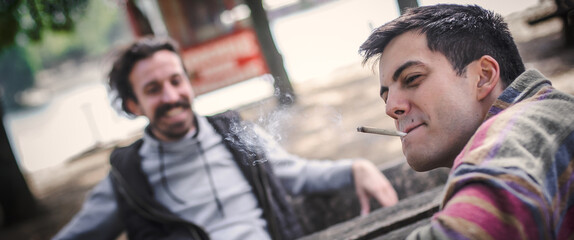 Two relaxed and happy young friends smoking marijuana ganja joint