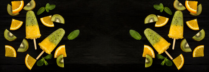 Banner. Top view of popsicles with kiwi and orange on the black wooden background. Copy space.