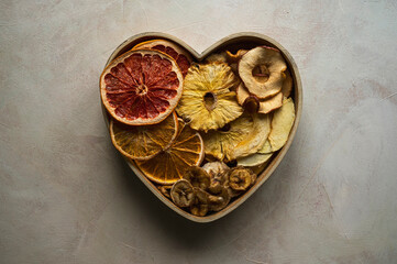 Dried fruit slices in heart shaped bowl. Dried orange, grapefruit, pineapples, banana. Healthy snack or dessert.