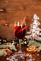A glass of mulled wine on the wooden table surrounded by Christmas decorations. Festive winter drink vertical photo