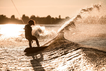 Amazing view of silhouette of female rider holding rope and rides down on wakeboard on splashing wave.