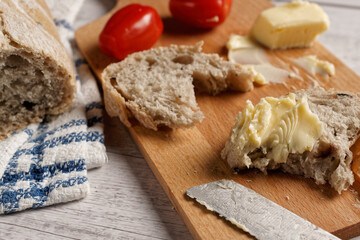 A slice of olive bread with butter, on a wooden cutting board. Next to it the cut loaf of bread.