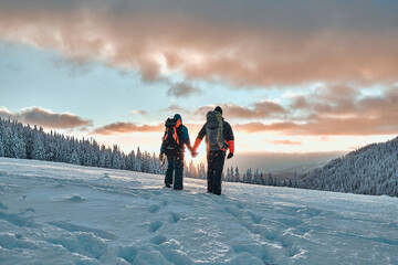 Rest in the mountains. Family couple holding hands and walking in the snowy pine mountains at...