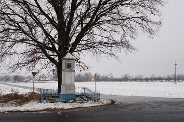 an old roadside shrine against a tree in the winter landscape of Poland 