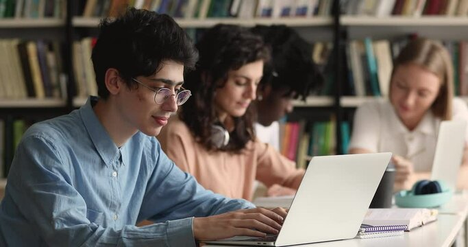 Student guy sit at table prepare for exam with laptop, writes essay, text coursework using computer sit at public or college library, makes research, do homework. Gen Z, modern tech, education concept