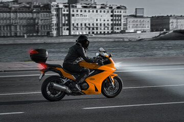 Fototapeta na wymiar A man rides a motorcycle in the city at night, no face. A motorcyclist rides along the embankment on an orange sports bike. Motorcycle travel. Headlights at night.
