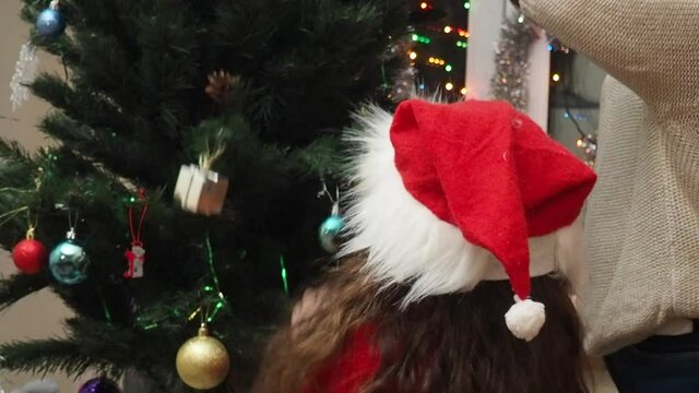 Family decorating a Christmas tree with boubles in the living room. mom and daughter decorate the tree with different toys home, family holidays, happy new year and christmas