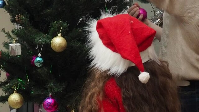 Family decorating a Christmas tree with boubles in the living room. mom and daughter decorate the tree with different toys home, family holidays, happy new year and christmas