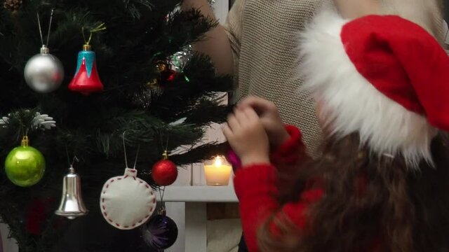 Family decorating a Christmas tree with boubles in the living room. mom and daughter decorate the tree with different toys home, family holidays, happy new year and christmas