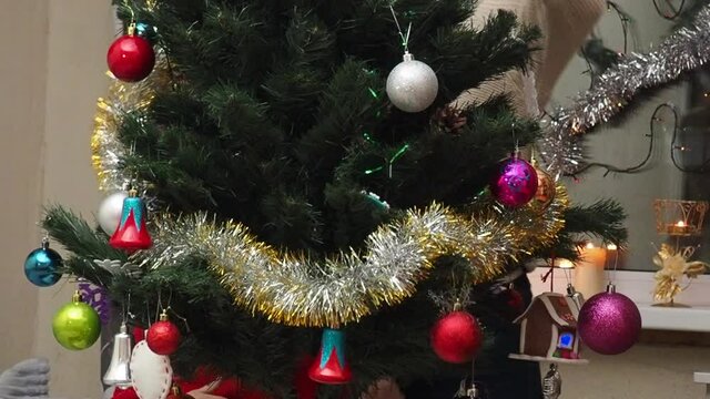 Family decorating a Christmas tree with boubles in the living room. mom and daughter decorate the tree with different toys home, family holidays, happy new year and christmas