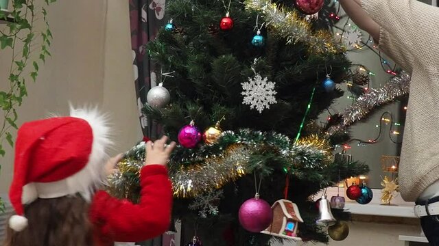 Family decorating a Christmas tree with boubles in the living room. mom and daughter decorate the tree with different toys home, family holidays, happy new year and christmas