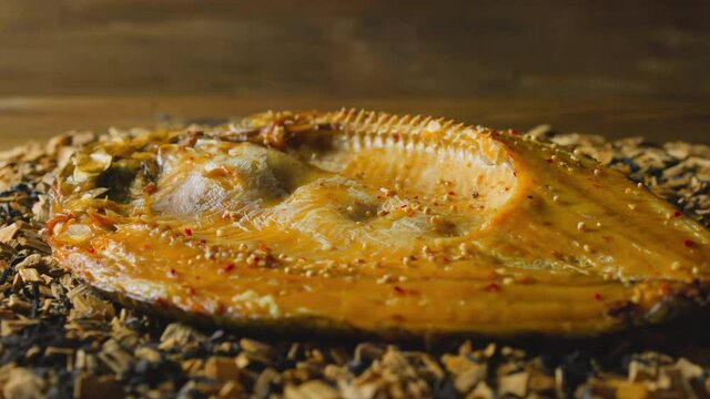 Tasty dressed ide fish with spicy seasonings and crust lies on pile of decayed wooden chips and charcoals in smokehouse close view slow motion
