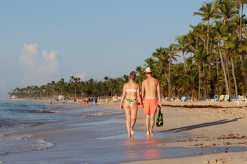 Young couple holding hands and walking by the sand on coconut palm trees background. Vacation on...