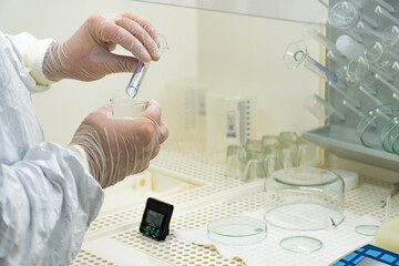 Scientist in protective white coat, mask and gloves analyzes a virus or bacteria sample in a...