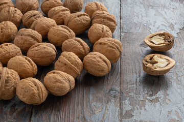 Two halves of a chopped walnut with a beautiful tasty kernel inside, ripe whole walnuts in shells are scattered nearby, on a vintage wooden background.