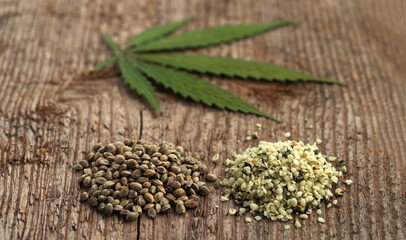 Two heaps of raw hemp seeds, whole and shelled, and cannabis leaf on a rough woody texture background. Selective focus.