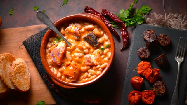 Traditional recipe of beans with chorizo and blood sausage called &ldquo;Fabada Asturiana&rdquo; on a dark table with some ingredients around. Typical Spanish food with &ldquo;compango&rdquo;. 