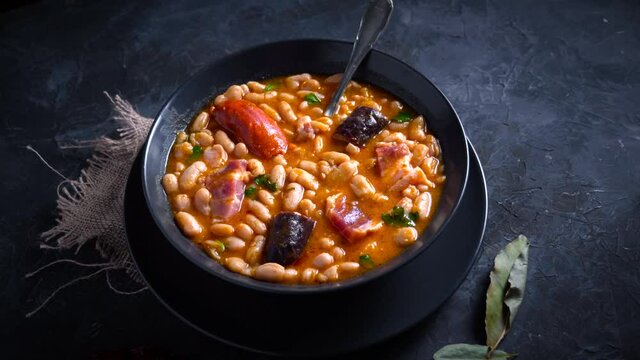 Traditional recipe of beans with chorizo and blood sausage called &ldquo;Fabada Asturiana&rdquo; on a dark table with some ingredients around. Typical Spanish food with &ldquo;compango&rdquo;. 