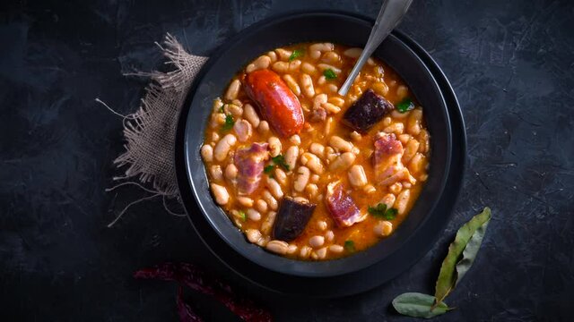 Traditional recipe of beans with chorizo and blood sausage called &ldquo;Fabada Asturiana&rdquo; on a dark table with some ingredients around. Typical Spanish food with &ldquo;compango&rdquo;. 
