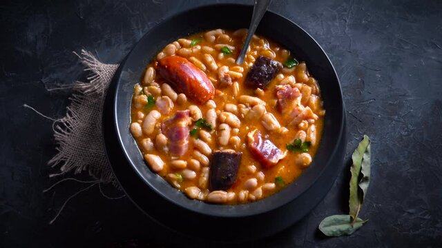 Traditional recipe of beans with chorizo and blood sausage called &ldquo;Fabada Asturiana&rdquo; on a dark table with some ingredients around. Typical Spanish food with &ldquo;compango&rdquo;. 