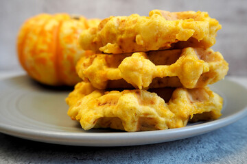 a close-up of three Belgian gluten- and lactose-free pumpkin waffles lies on a wooden board next to slices of dried orange and a small pumpkin on a blue wooden table background