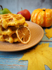 Belgian gluten-free pumpkin waffles lie on a gray plate with a dry slice of lemon, pear, apple and anise stars on a blue wooden table. maple leaves