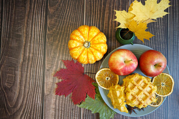 Belgian gluten-free pumpkin waffles lie on a gray plate with a dry slice of lemon, an apple and anise stars on a wooden table. top view