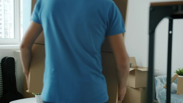 Young cheerful woman is unpacking belongings while mover is bringing cardboard boxes to new house. Relocation and service concept.
