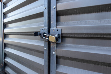 Angled view of a yellow padlock keeping two large metal doors locked up tight in an outdoor storage...