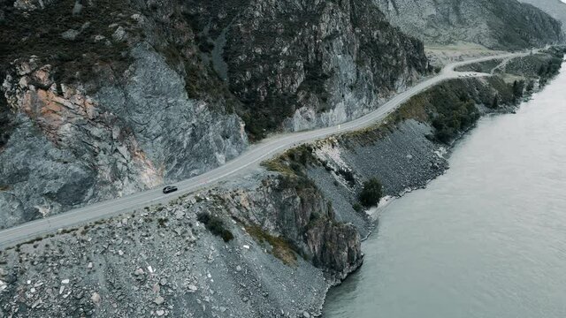 Dark grey car drives through narrow road in the mountains. Drone footage