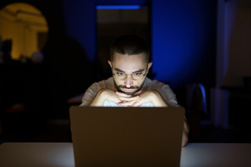 Pensive young freelancer journalist or writer work on publication late at night reading and editing text on laptop to finish project within deadline. Male freelance worker sitting at computer overtime
