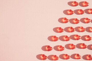 Shiny red soft candy hearts pattern against pastel pink background. Romantic minimal concept