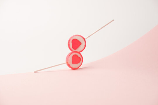 Two heart themed lolipops touching in the air over the two tone pastel pink background. Romance minimal concept